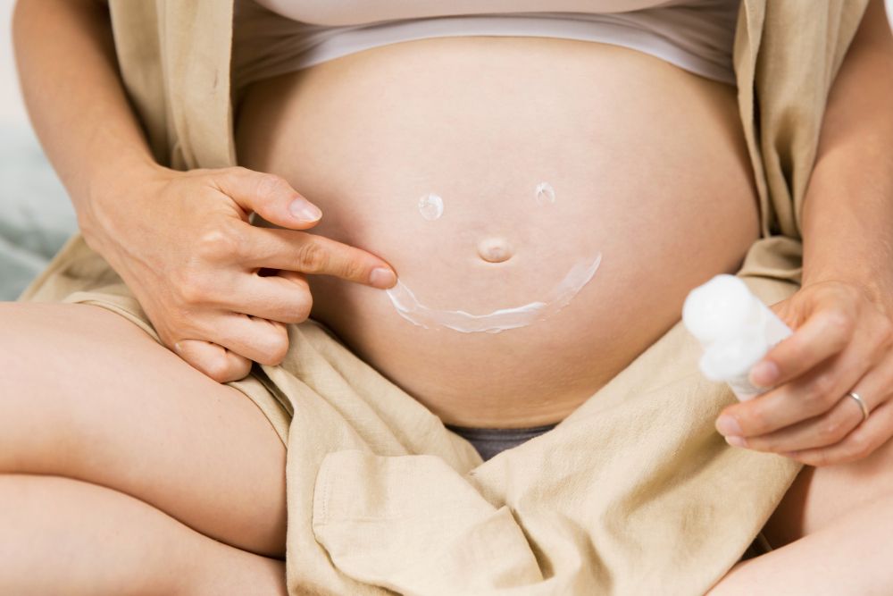 A pregnant woman drawing a radiant smile on her belly, ensuring safe facial treatments during pregnancy in Singapore.